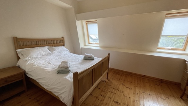 Bright bedroom with wooden bed and sloped window wall