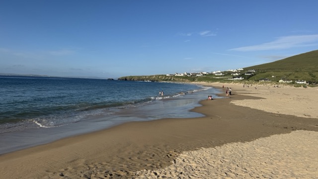 Dugort beach with clear blue water and people walking along the sand