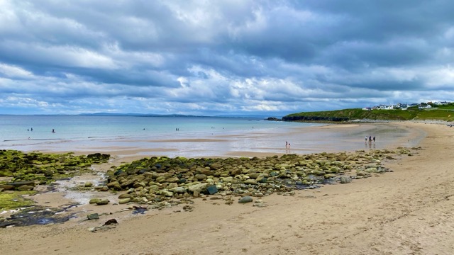 Rocky shoreline and sandy beach at Dugort under dramatic clouds